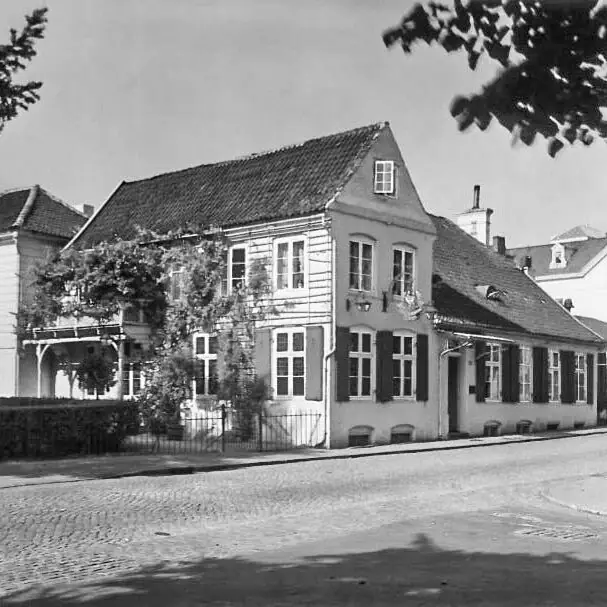 Altes Foto Louis C. Jacob Hotel Hamburg Ein altes Schwarz-Weiß-Foto vom Louis C. Jacob Hotel mit einem Zaun und einer Hecke davor.